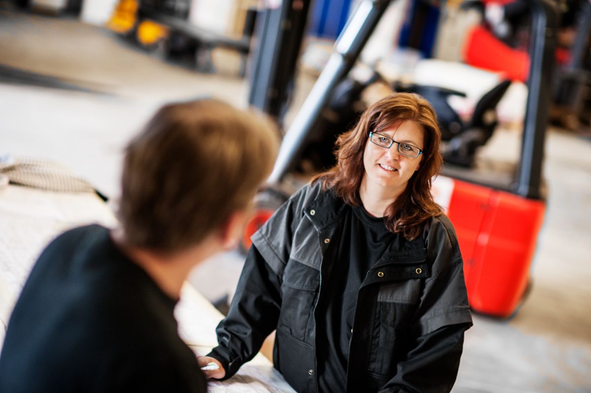 A manager in a warehouse talking with an employee at a table